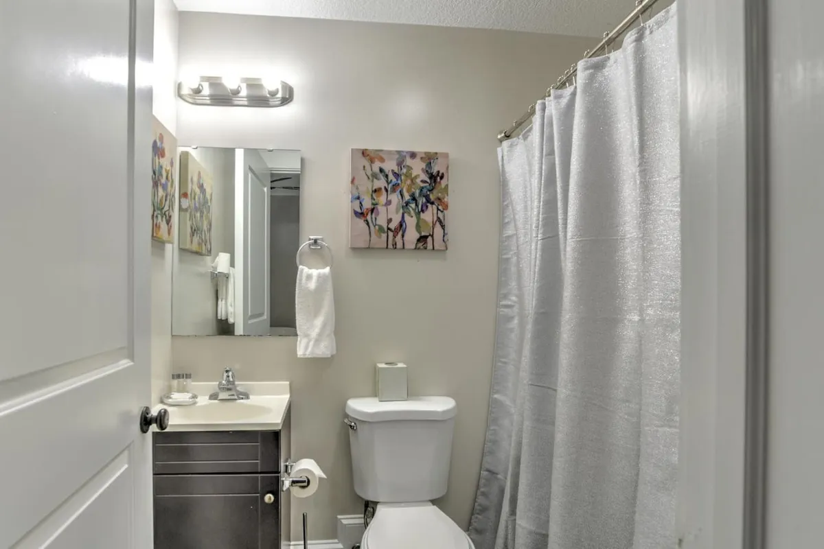 A modern bathroom featuring colorful artwork, a bright and clean shower area, and a contemporary sink. The space feels calm and refreshing, offering a touch of artistry and tranquility for morning and evening routines.
