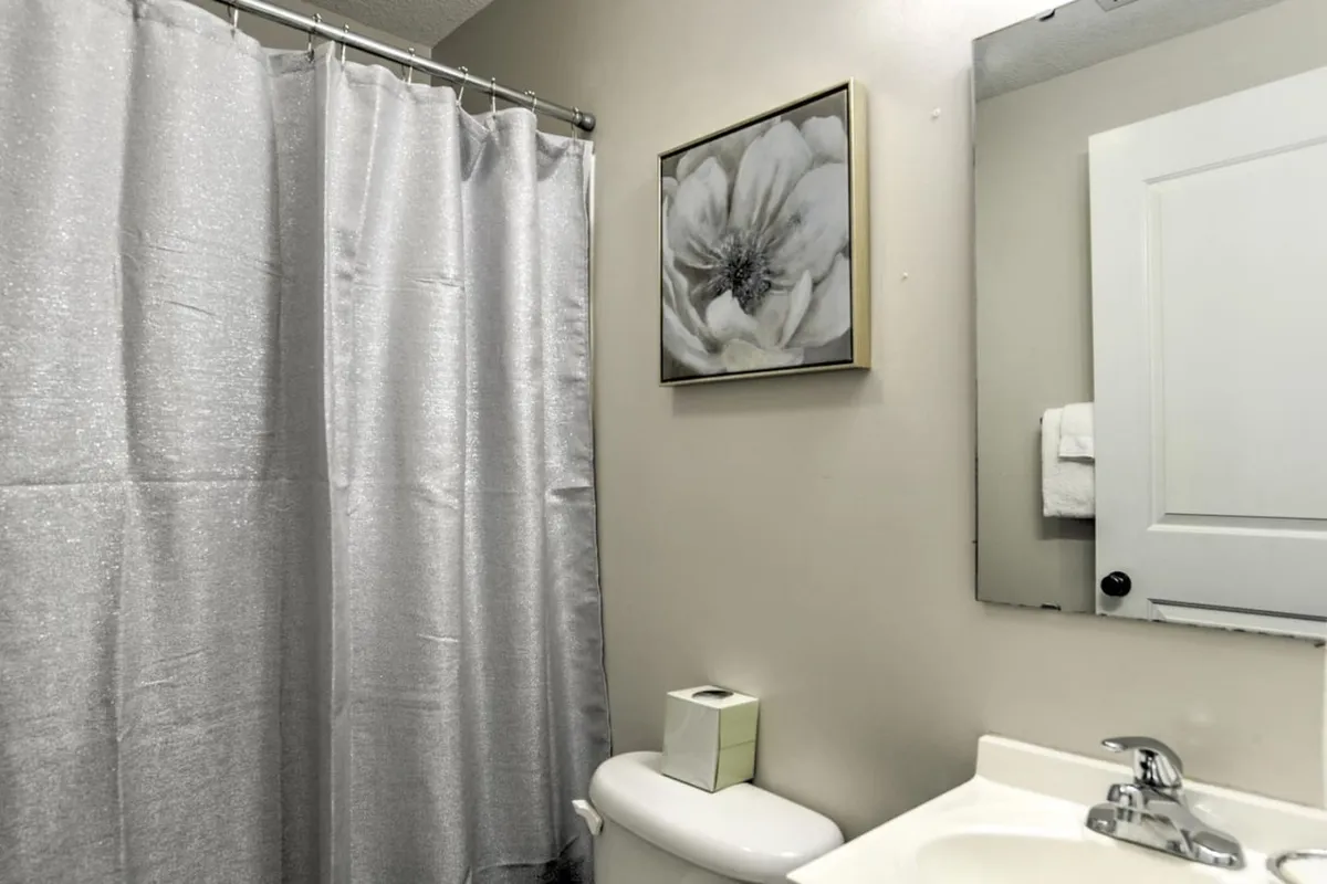 A modern bathroom featuring a fresh shower curtain, framed floral artwork, a sleek sink, and ample natural light. The space feels serene and inviting, ideal for relaxing showers and personal care routines.