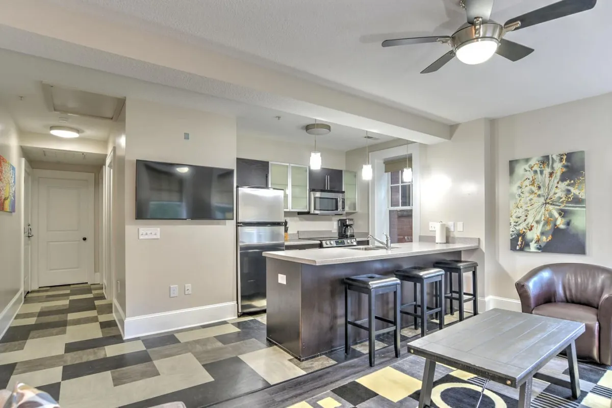 This image showcases the condo’s open-concept living space, featuring a stylish kitchen island with modern stools, an inviting living area with plush seating, and tasteful wall art that adds character and warmth. The scene is bathed in natural light, creating a welcoming and sociable atmosphere perfect for gatherings or relaxing downtime.