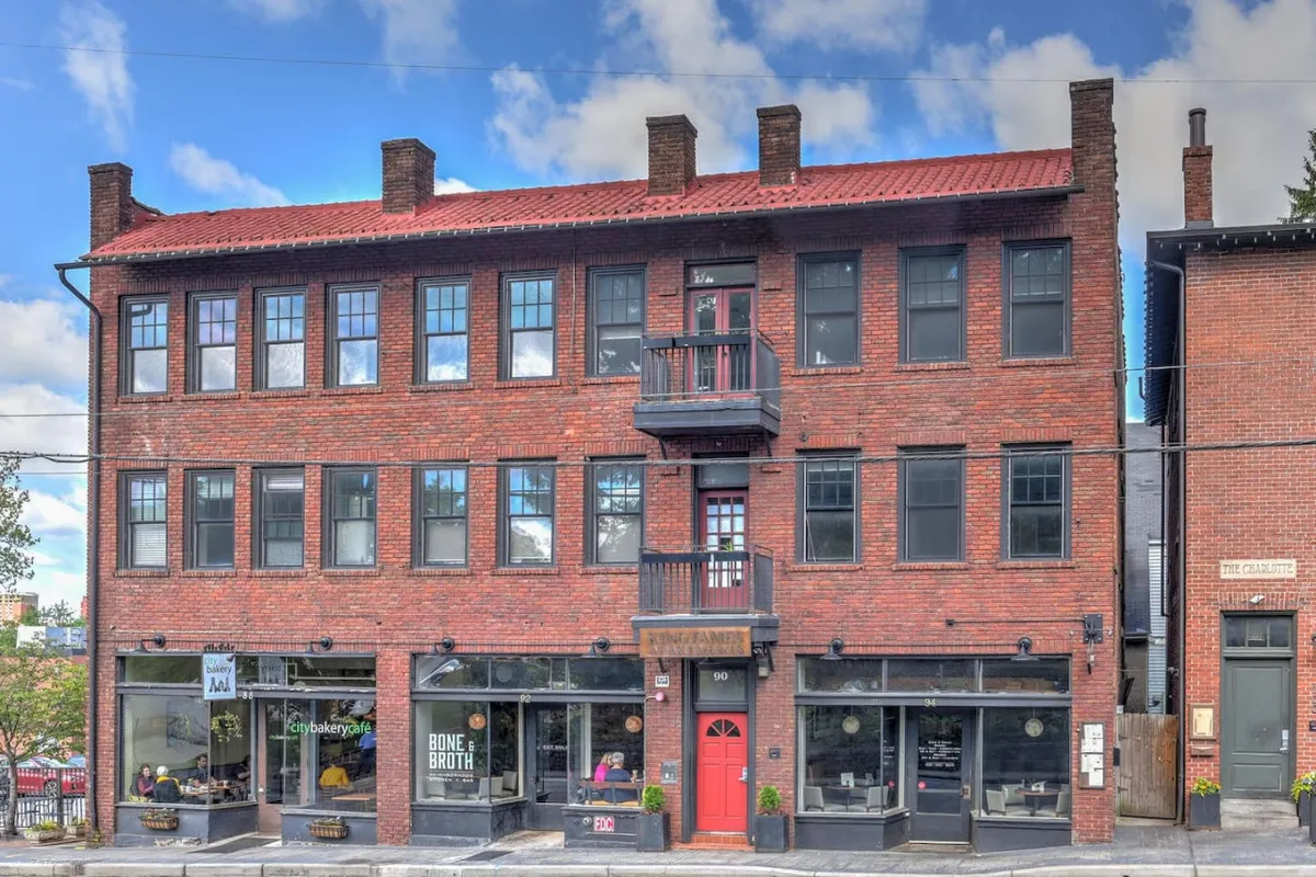 Another exterior shot, this image showcases the building's welcoming red door, brick facade, balcony, and nearby storefronts. The image conveys a sense of arrival and hints at the convenience of unassigned parking and easy access to the vibrant street life.