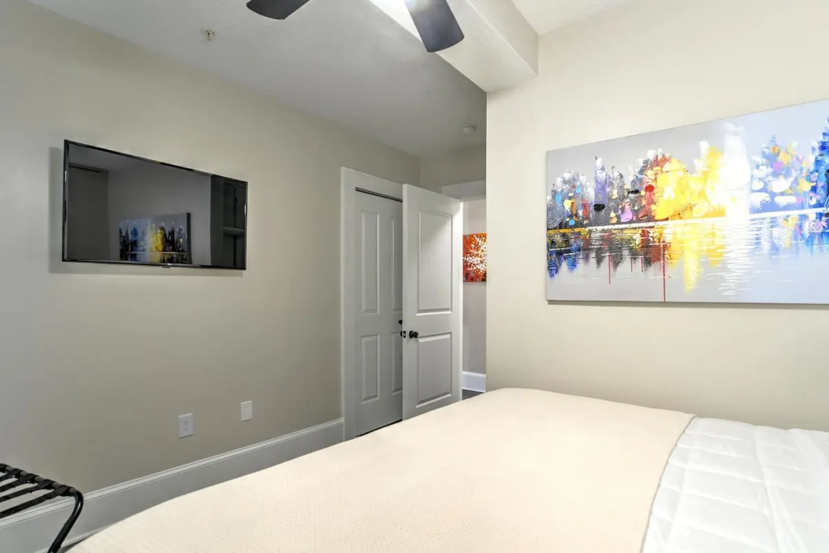 An interior view featuring a stylish bedroom with a cozy bed, abstract artwork, a television, and a doorway. The third-floor aspect provides a sense of privacy and retreat from the street below, matching the section’s focus on a quiet, comfortable haven within the city.