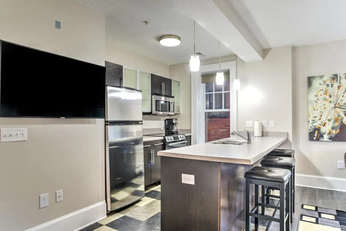 A bright, open kitchen with a spacious island surrounded by bar stools, gleaming stainless steel appliances, and modern artwork on the wall. The setup is ideal for both everyday cooking and entertaining, with natural light accentuating the contemporary finishes and inviting atmosphere.