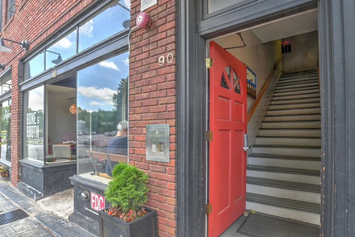 A welcoming exterior view of the King James Building, featuring a distinct red door, large windows, brick facade, and a prominent staircase ascending from the street. The image captures the inviting entryway and hints at the building's historic character.